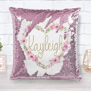 May include: A decorative sequin pillow in shades of pink. The pillow features a floral heart design with the name "Kayleigh" in gold script. The pillow is a square shape and is likely used for home decor.