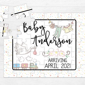 May include: A white jigsaw puzzle with a colorful confetti pattern. The puzzle features a stork carrying a baby, a train, and a clothesline with baby clothes. The text on the puzzle reads "Baby Anderson Arriving April 2021".