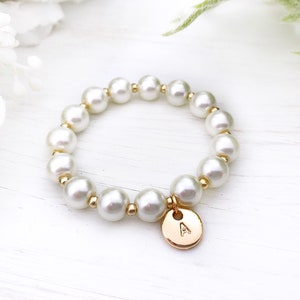 May include: A white pearl bracelet with a gold charm featuring the letter 'A'.