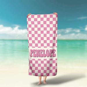 May include: Pink and white checkered beach towel with the name Penelope in pink letters.
