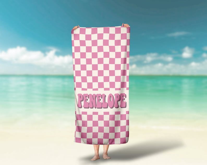 May include: Pink and white checkered beach towel with the name Penelope in pink letters.