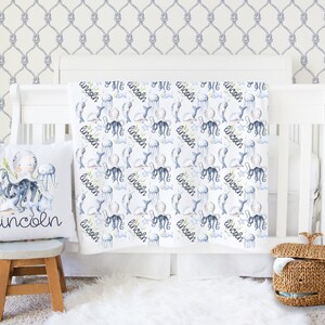 May include: A white baby blanket with a nautical theme featuring an octopus, jellyfish, and the name "Lincoln" repeated throughout the design. The blanket is displayed on a white crib with a gray rope pattern wallpaper.