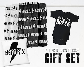 Może przedstawiać: Biało-czarny śpioszek dla niemowlęcia z napisem "Born to Rock" i graficznym błyskawicą. Biała poduszka z czarnym błyskawicą i napisem "Hendrix" oraz dwa czarno-białe ręczniki z napisem "Hendrix" i graficznym błyskawicą. Napis "Ultimate Born to Rock Gift Set" jest wydrukowany czarnym kolorem na białym tle.