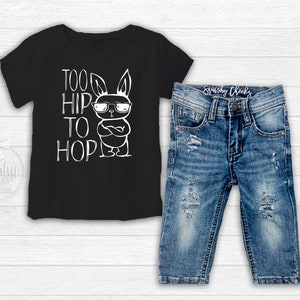 Black boy easter shirt adorned with a funny graphic featuring a bunny wearing sunglasses and text saying too hip to hop with distressed denim jeans