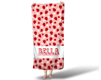 May include: Pink beach towel with a white border and a pattern of red strawberries and white flowers. The name "BELLA" is printed in a retro font on the white border.