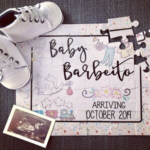 May include: A white puzzle with colorful polka dots and a baby announcement. The puzzle says "Baby Barbeiro" and "Arriving October 2019". There are baby shoes and an ultrasound image on the puzzle.