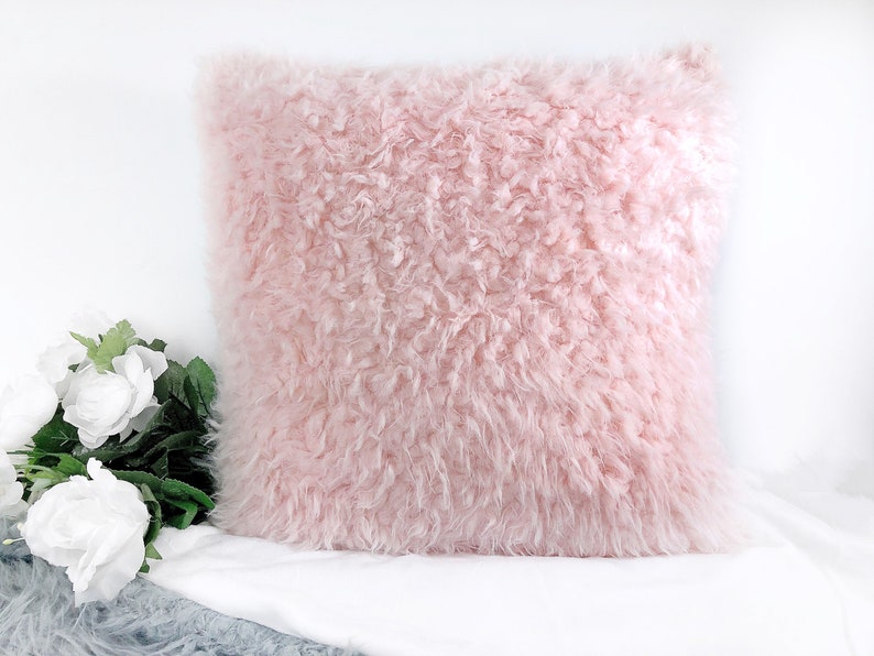 Op de afbeelding: Een zacht, pluche roze kussen met een donzige textuur. Het kussen is gemaakt van imitatiebont en perfect om elke kamer een vleugje luxe te geven.