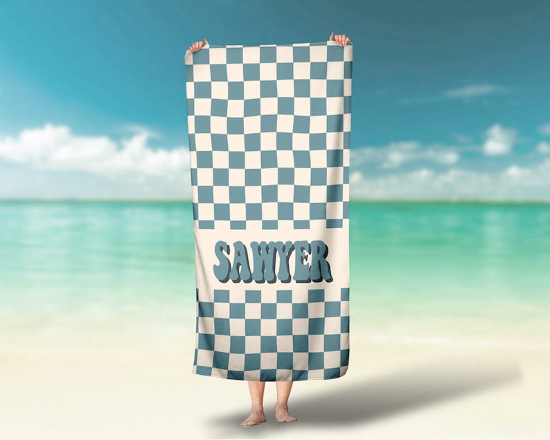 May include: A blue and white checkered beach towel with the name "Sawyer" printed in blue letters.