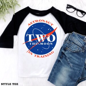 May include: A white and black raglan style tee shirt with a blue and red NASA-inspired logo that says "Astronaut Two The Moon In Training".