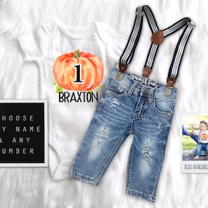 May include: A white onesie with a watercolor pumpkin and the number 1, the name Braxton is printed below the pumpkin. A pair of blue denim overalls with suspenders and a white and navy stripe pattern. A black letter board with the text "Choose any name & any number". A photo of a baby boy wearing a similar onesie and overalls. The text "Also available in shorts" is printed below the photo.