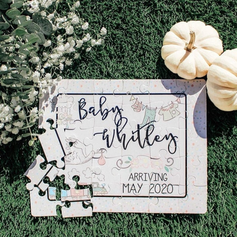 May include: A white jigsaw puzzle with a pink and blue floral design. The puzzle is partially assembled and features the text "Baby Whitley Arriving May 2020".