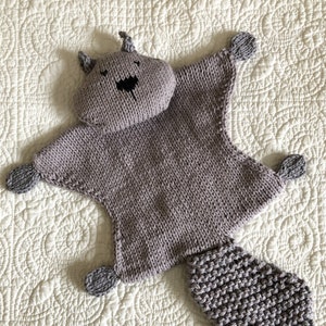 Könnte beinhalten: Ein graues, gestricktes Plüschtier in Form eines Eichhörnchens mit einem langen Schwanz. Das Spielzeug hat ein einfaches, schwarzes gesticktes Gesicht.