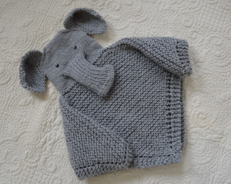 May include: A gray knitted sweater with an attached elephant-shaped hood. The hood has a gray knitted trunk and ears.