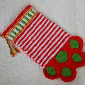 May include: Red and white striped knitted stocking with a green and yellow trim and a green paw print design.
