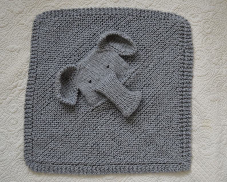 May include: A gray knitted baby blanket with a gray knitted elephant applique. The blanket has a diamond pattern and a border.