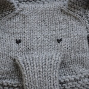 May include: Gray knitted fabric with a textured pattern, resembling an elephant's face with two black eyes.