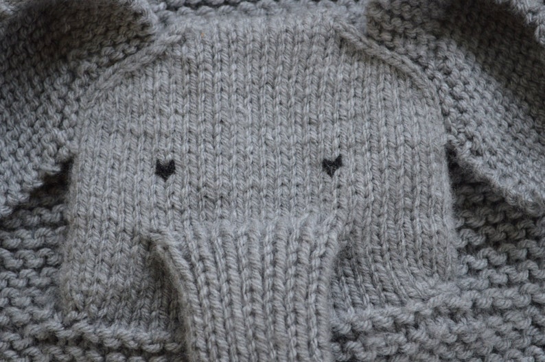May include: Gray knitted fabric with a textured pattern, resembling an elephant's face with two black eyes.