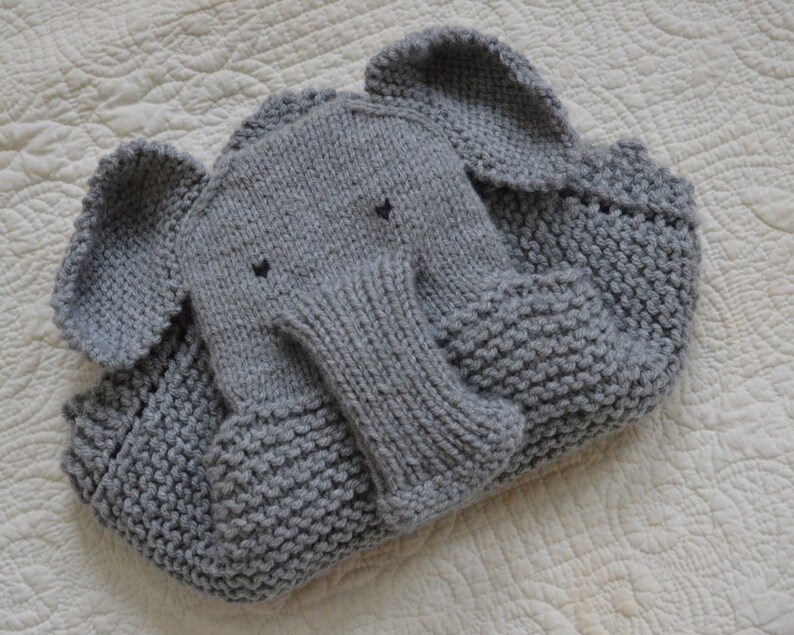 May include: A gray knitted elephant blanket with a textured surface. The blanket is folded and the elephant's trunk is visible.
