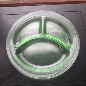 May include: A round, light green glass serving plate featuring three distinct sections. The plate has a smooth, translucent finish with a textured, cross-hatched pattern along the outer rim, creating a clear division between the central compartments.