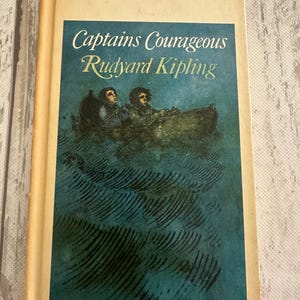 May include: A vintage hardcover book titled "Captains Courageous" by Rudyard Kipling. The cover features a teal illustration of two people in a boat on wavy water. The book has a cream-colored spine and cover with the price tag in the upper right corner.