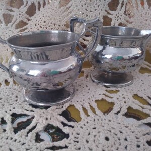May include: A silver creamer and sugar bowl set with a hammered finish. The set is on a white crocheted doily.