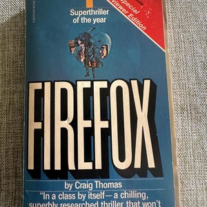 May include: A vintage paperback book titled "FIREFOX" by Craig Thomas. The cover is predominantly blue with the title in large white letters. It features a graphic of a person in a helmet and the text "Superthriller of the year". A red banner reads "Special Previewer Edition".