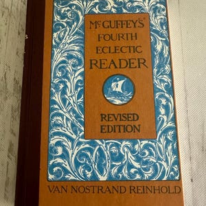 May include: A vintage book titled "McGuffey's Fourth Eclectic Reader, Revised Edition." The cover is a warm brown with a blue and white ornate design. The book's spine is a deep burgundy, and the publisher is Van Nostrand Reinhold.