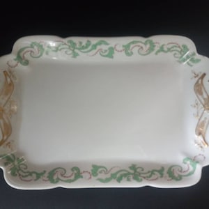 May include: A white rectangular serving tray with a green and gold floral design around the edge. The tray has two handles on the sides.
