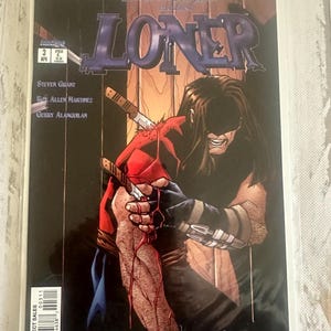 May include: Comic book cover for "Loner" featuring a dark-haired character with knives in their arm. The title is in large purple letters. The cover has a dark, dramatic tone with the text "Wildstorm Spotlight" at the top.