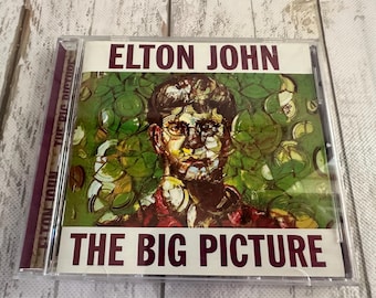 May include: CD case for Elton John's album, "The Big Picture." The cover features a portrait of Elton John with green and white abstract shapes. The album title and artist's name are in maroon text.