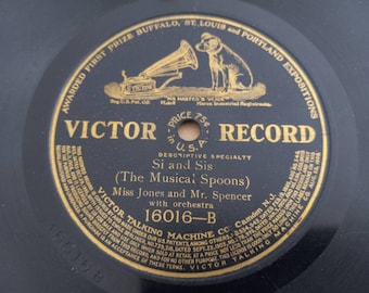 Può includere: Un'etichetta disco Victor nera e dorata con il testo "Victor Record" in un grande carattere grassetto. L'etichetta presenta anche il testo "Si and Sis (The Musical Spoons)" e "Miss Jones and Mr. Spencer with orchestra". Il numero del disco è 16016-B.