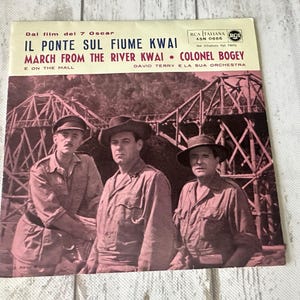 May include: Vintage vinyl record album cover for "Il Ponte Sul Fiume Kwai" featuring a sepia-toned image of three men in military attire. The album title and artist information are printed in Italian and English.