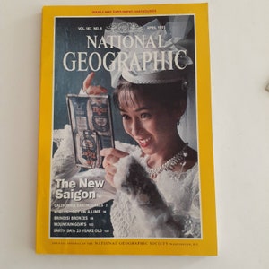 May include: A vintage April 1995 National Geographic magazine with a yellow border. The cover features a woman holding a Tiger beer can, with the title "The New Saigon." Additional text includes articles on earthquakes, koalas, and mountain goats.
