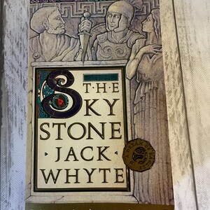 May include: A book cover with a medieval illustration of three people. The title is "The Sky Stone" by Jack Whyte. The book cover is gold and brown with a green and blue border.
