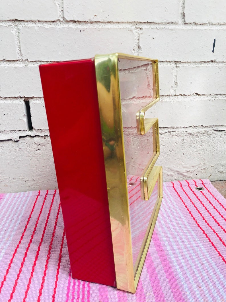 May include: A red and gold vintage sign with the letter "E" in a clear glass panel. The sign is made of metal and has a rectangular shape.