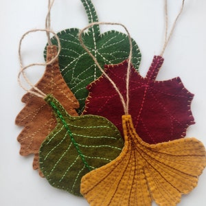 Puede incluir: Cinco adornos de hojas de fieltro en varios colores, incluyendo verde, marrón, rojo y amarillo. Cada hoja tiene un lazo de cuerda para colgar.