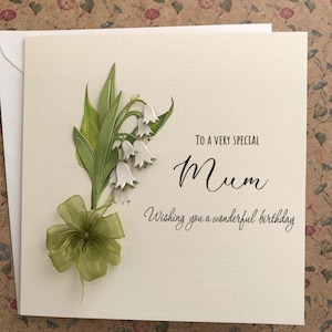 May include: A white card with a green and white lily of the valley flower design. The card says "To a very special Mum Wishing you a wonderful birthday."