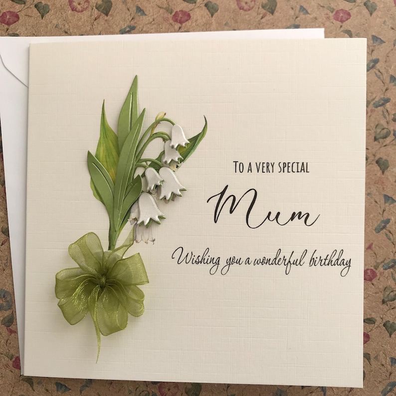 May include: A white card with a green and white lily of the valley flower design. The card says "To a very special Mum Wishing you a wonderful birthday."