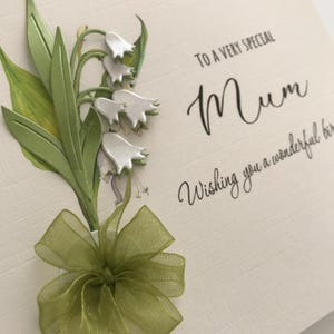 May include: A white card with a green and white lily of the valley flower design. The card says "To a very special Mum Wishing you a wonderful birthday".