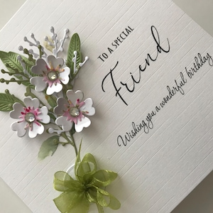 Może przedstawiać: Biała kartka z zielonymi i białymi kwiatami i zieloną kokardką. Na kartce napisano "To a special Friend Wishing you a wonderful birthday".