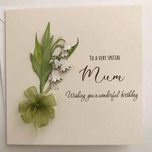 May include: A white card with a green and white lily of the valley flower design. The card says "To a very special Mum Wishing you a wonderful birthday."