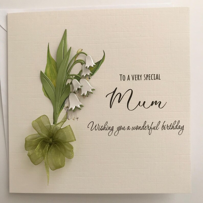 May include: A white card with a green and white lily of the valley flower design. The card says "To a very special Mum Wishing you a wonderful birthday."