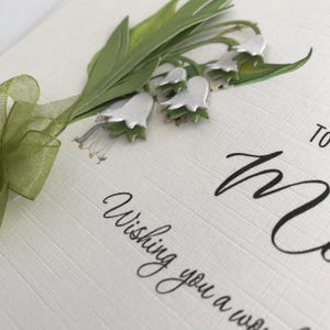 May include: A white card with green leaves and white flowers. The card says "Wishing you a wonderful" and "To Mum".