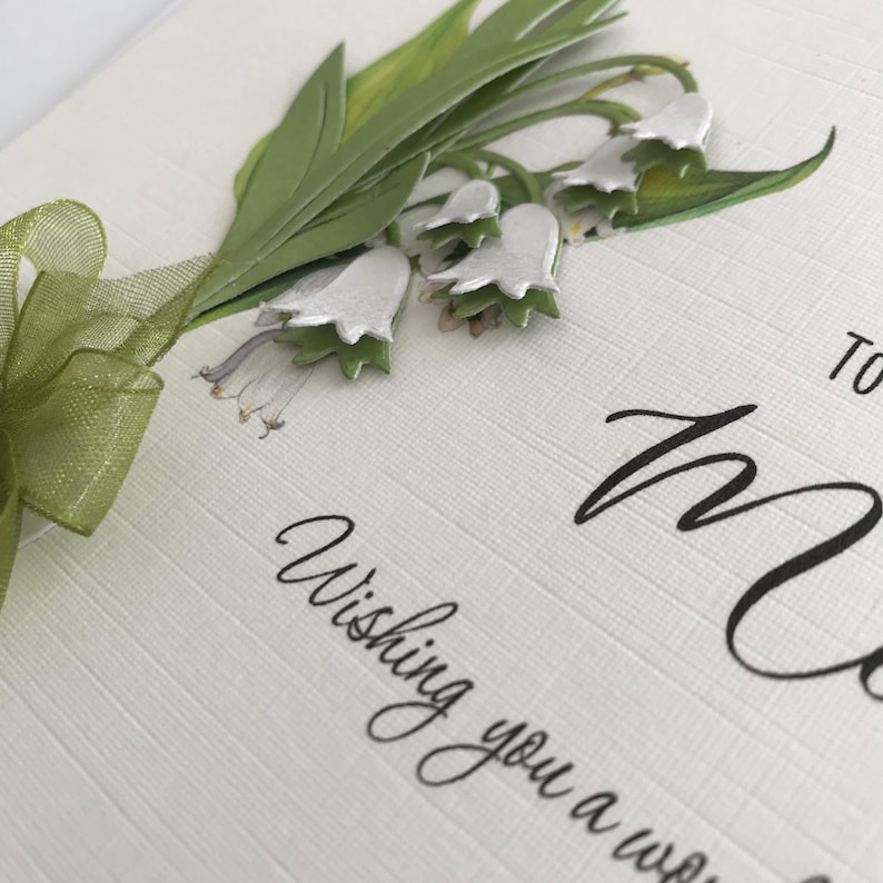 May include: A white card with green leaves and white flowers. The card says "Wishing you a wonderful" and "To Mum".
