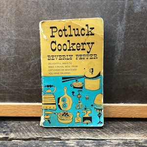 May include: A yellow and blue vintage cookbook titled "Potluck Cookery" by Beverly Pepper. The cover features illustrations of various kitchen utensils and food.