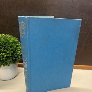 May include: A hardcover book titled "A COSIDERWALK" by Catherine Marshall. The book has a light blue cover with gold lettering. The book is standing upright on a light-colored surface.