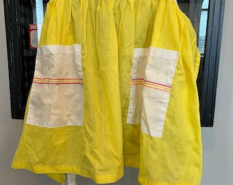 May include: A yellow apron with white pockets and white ties. The pockets have red, orange, and yellow stripes.