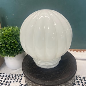 May include: A spherical white glass light fixture shade featuring a vertical ribbed pattern. The globe has a smooth, translucent finish and a circular opening at the base for mounting, designed to diffuse light evenly across a room.
