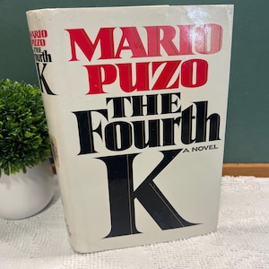May include: A hardcover book titled "The Fourth K" by Mario Puzo. The book cover is off-white with red and black lettering. The title is prominently displayed, with the author's name at the top.