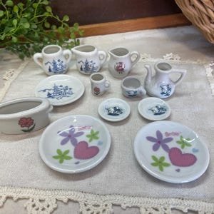 May include: A miniature tea set with a white background and blue and pink floral designs. The set includes a teapot, creamer, sugar bowl, cups, saucers, and plates.